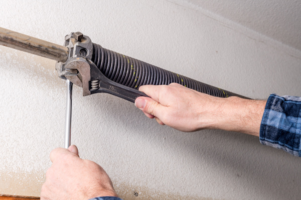 Home repairman uses tools to work on a garage door spring
